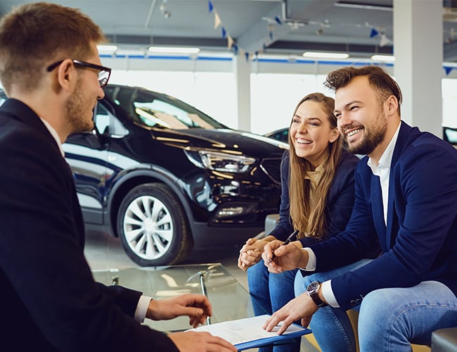 Man and woman talking to salesman in car dealership