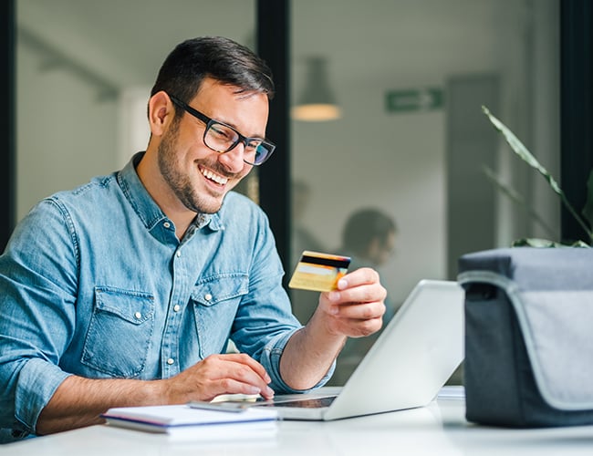 May sitting at desk in office paying for online order using debit card