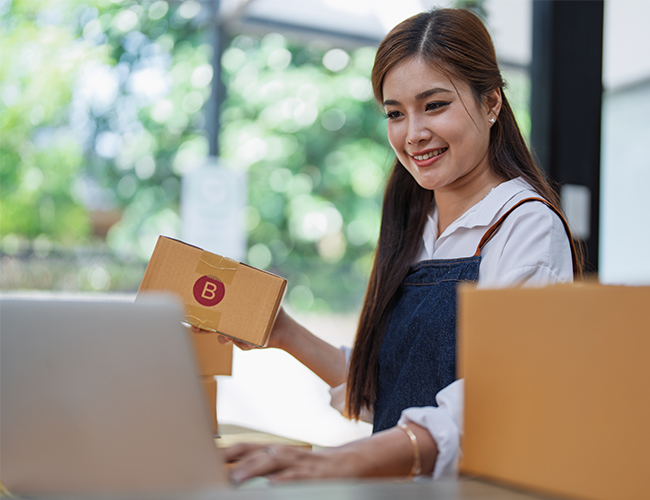 Smiling woman wearing apron holding inventory looking at laptop