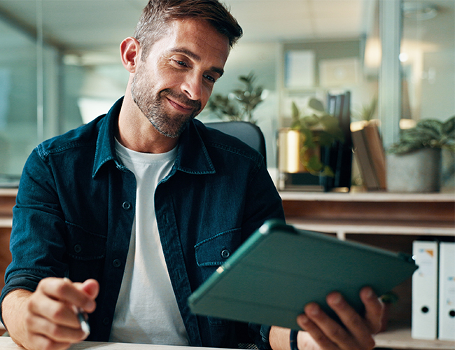 Smiling relieved man looking at tablet while doing bookwork in office