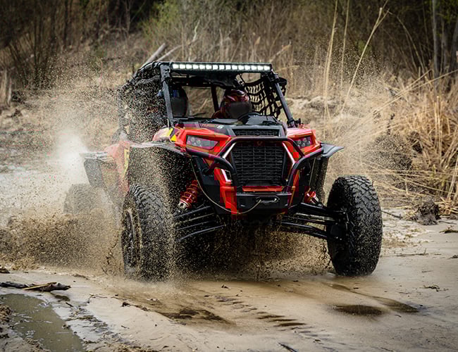 Red UTV driving through mud and water in field Red UTV driving through mud and water in field