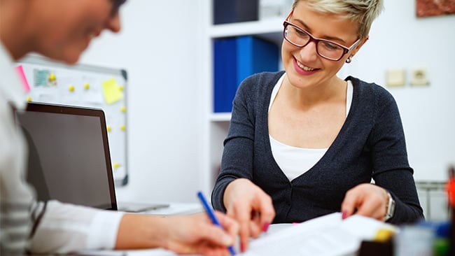 Woman explaining paperwork across desk while smiling