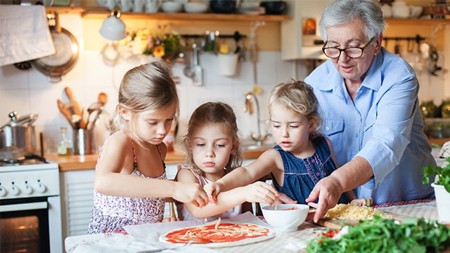 Grandmother making homemade pizza with granddaughters