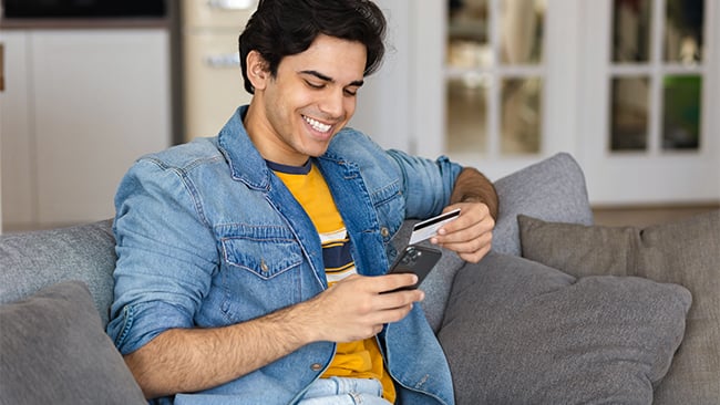Young Adult man on couch, online shopping with his phone and VISA credit card Young Adult man on couch, online shopping with his phone and VISA credit card